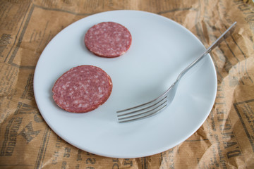two slices of sausage and a fork on a plate and a newspaper