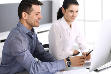 Obraz premium Cheerful smiling businessman and woman working with computer in modern office. Headshot at meeting or workplace. Teamwork, partnership and business concept