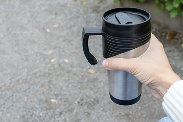 Woman holding a metal thermo cup with hot drink, tea or coffee, copy space