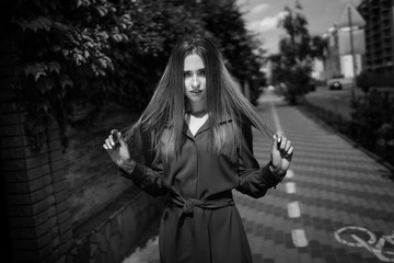 Black and white photo of attractive woman wearing dress on a road background. Long hair. Portrait of a beautiful girl. Young female photosession.