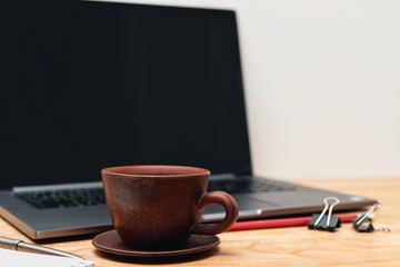 Work wooden office table with laptop, coffee cup, notepad and pen