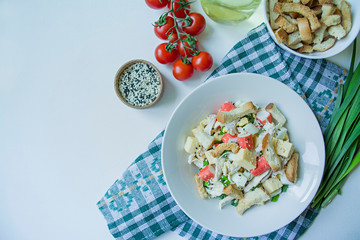 Salad with crackers, crab sticks, chicken fillet, fresh herbs and hard cheese seasoned with mayonnaise butter served in a white plate. Salad with mayonnaise. View from above. White background.