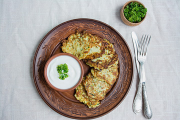 Zucchini fritters, vegetarian zucchini pancakes, served with fresh herbs and sour cream, top view. Light background.