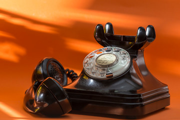 old telephone of black color, retro telephone on orange background