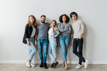 Happy intercultural guys and girls in casualwear standing against white wall