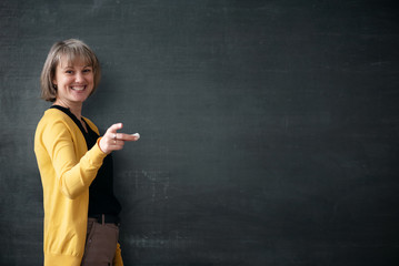 Fototapeta Young teacher with piece of chalk is standing near blackboard in a classroom. obraz