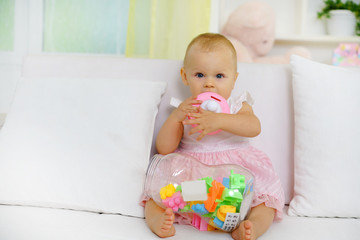 Sweet baby girl playing with toys on sofa, looking at camera             