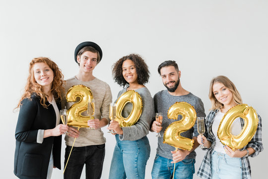 Young joyful friendly people holding number of new year and flutes with chamagne