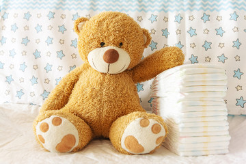 diapers with baby soft toy bear on the background of the nursery and crib, the concept of using...