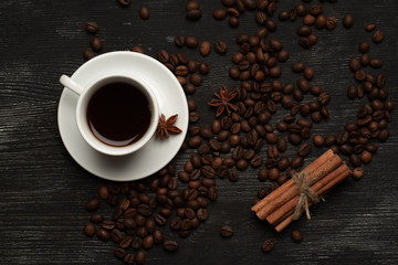White cup with coffee sticks of cinnamon and anise on a black background with coffee beans and place for text top view