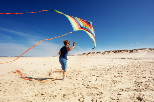 Boy run with color striped kite on the sand beach