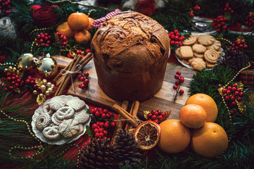 Christmas ingredients table with a Panettone in the center on a wooden board, accompanied by...