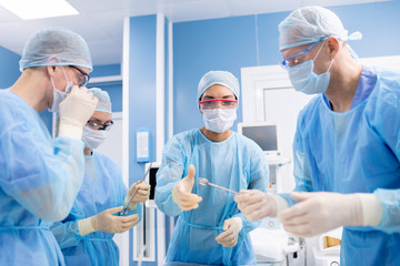 Group of four professionals in protective uniform taking surgical instruments