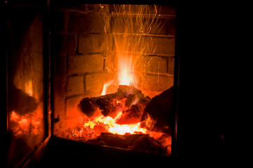 sparks in a fireplace with firewood on a black background, holiday of lights, christmas, horizontal