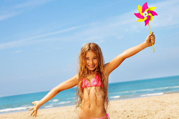 Happy girl smile in bikini on beach with pinwheel - obrazy, fototapety, plakaty