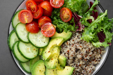 Close up of budha bowl with quinoa, avocado, cucumber, salad, tomatoe, olive oil. Clean eating, diet food. Dark background.