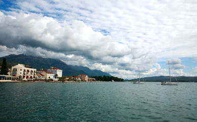 Fototapeta premium Bay in seaside town with boats, houses in green mountains on blue sky,.Tivat, Montenegro