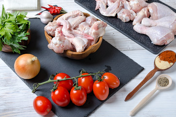raw chicken wings and chicken thighs, ingredients for cooking, seasoning vegetables and chicken on a wooden table, 45 view
