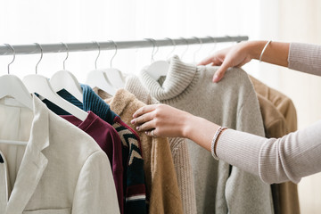 Hands of young female shopper choosing warm knitted and woolen clothes