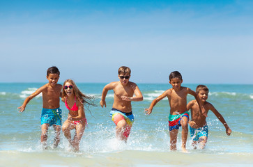 Group of kids running from the sea with splashes