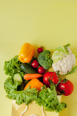Organic vegetables broccoli cucumbers bell peppers apples in brown paper Kraft grocery bag on yellow background. Healthy diet dietary fiber vegan plastic free concept. Poster banner