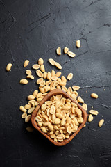 Wooden bowl with roasted peeled peanuts, salty beer snack on dark background with copy space, top view