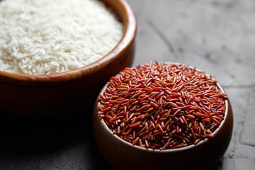 Red and white rice in a wooden bowls on black stone table. Dry uncooked grains. Ingredient for cooking various dishes