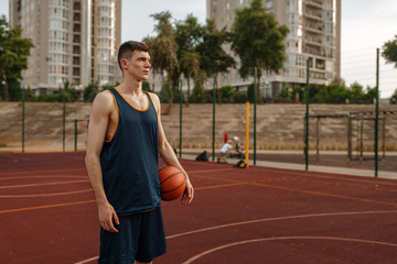 Male basketball player holds a ball, outdoor court © Nomad_Soul
