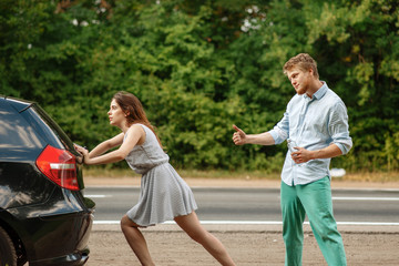 Young couple pushing broken car on road, breakdown