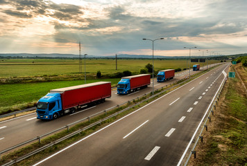 Lorry trucks in line as a caravan or convoy  on country highway under a beautiful sky - obrazy, fototapety, plakaty
