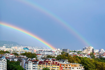 Gorgeous double rainbow over city. A double rainbow appeared against gray stormy sky over residential area of the city.