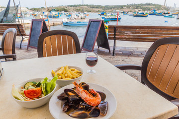 Sea food dish with fries and salad in a retaurant in the harbor of Marsaxlokk town, Malta - obrazy, fototapety, plakaty