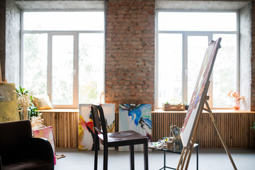 Wooden chair of painter, easel with unfinished painting and other arts stuff