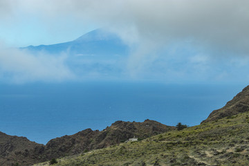 View of Tenerife through low clouds. Parque Natural Majona. Northeastern part of La Gomera Island. Old volcanic mountains covered by green grass, laurels and heather on steep slopes. Canary Islands