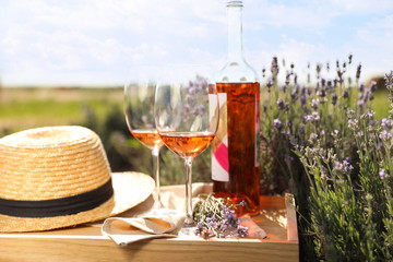 Bottle and glasses of wine on wooden table in lavender field
