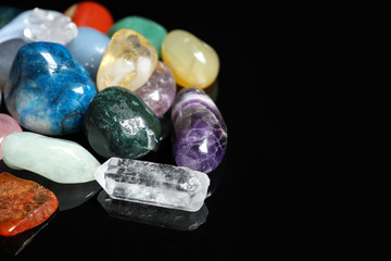 Different beautiful gemstones on black background, closeup. Space for text