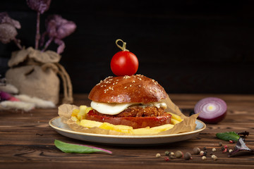 cheeseburger decorated with cherry tomato on a plate on a wooden table