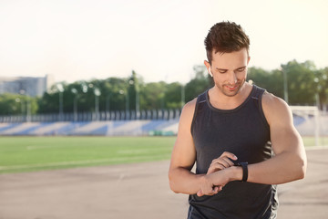 Young sportsman with wireless earphones and smart watch at stadium