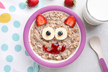 Tasty porridge served with berries, jam and milk on marble table, flat lay. Creative idea for kids breakfast