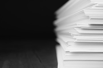 Stack of blank paper on grey stone table against dark background. Space for text