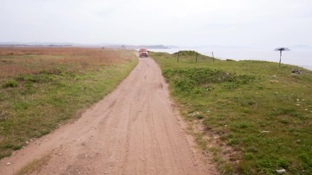 Summer, 2019 - Primorsky Krai, Russia - Orange expedition minibus Sable driving along a dusty dirt road among green fields.