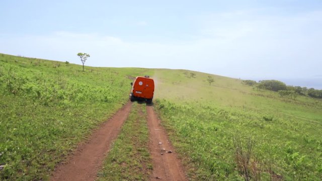 Summer, 2019 - Primorsky Krai, Russia - Orange expedition minibus Sable driving along a dusty dirt road among green fields.