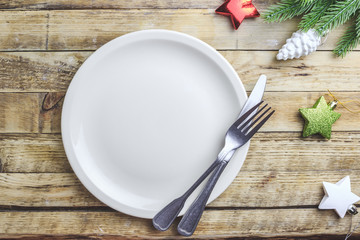 Rustic christmas table setting from above. Elegant empty light beige plate, cutlery, gift box and fir branch on rustic wooden background. Top view