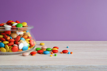 Multi-colored candies. Round candies  in a glass jar on a white table. Lilac background