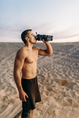 Male athlete drinks water after workout in desert