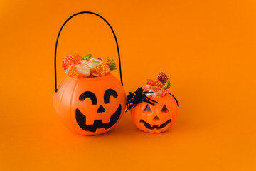 trick or treat for halloween. Pumpkin bucket with sweets and spiders on an orange background. Sweets for kids for Halloween. Copyspace - obrazy, fototapety, plakaty