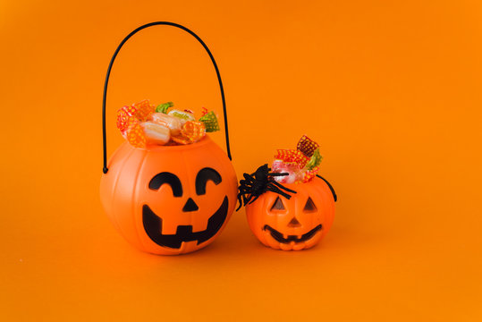 trick or treat for halloween. Pumpkin bucket with sweets and spiders on an orange background. Sweets for kids for Halloween. Copyspace