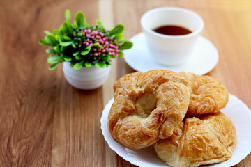 Fresh croissant with coffee cup on a wooden table.