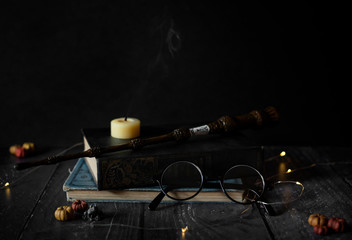 magic wand and spell books on desk with glasses, smoking candle, and other witch items, wizards desk, halloween theme, vintage books