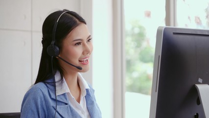 Customer support agent or call center with headset works on desktop computer while supporting the...